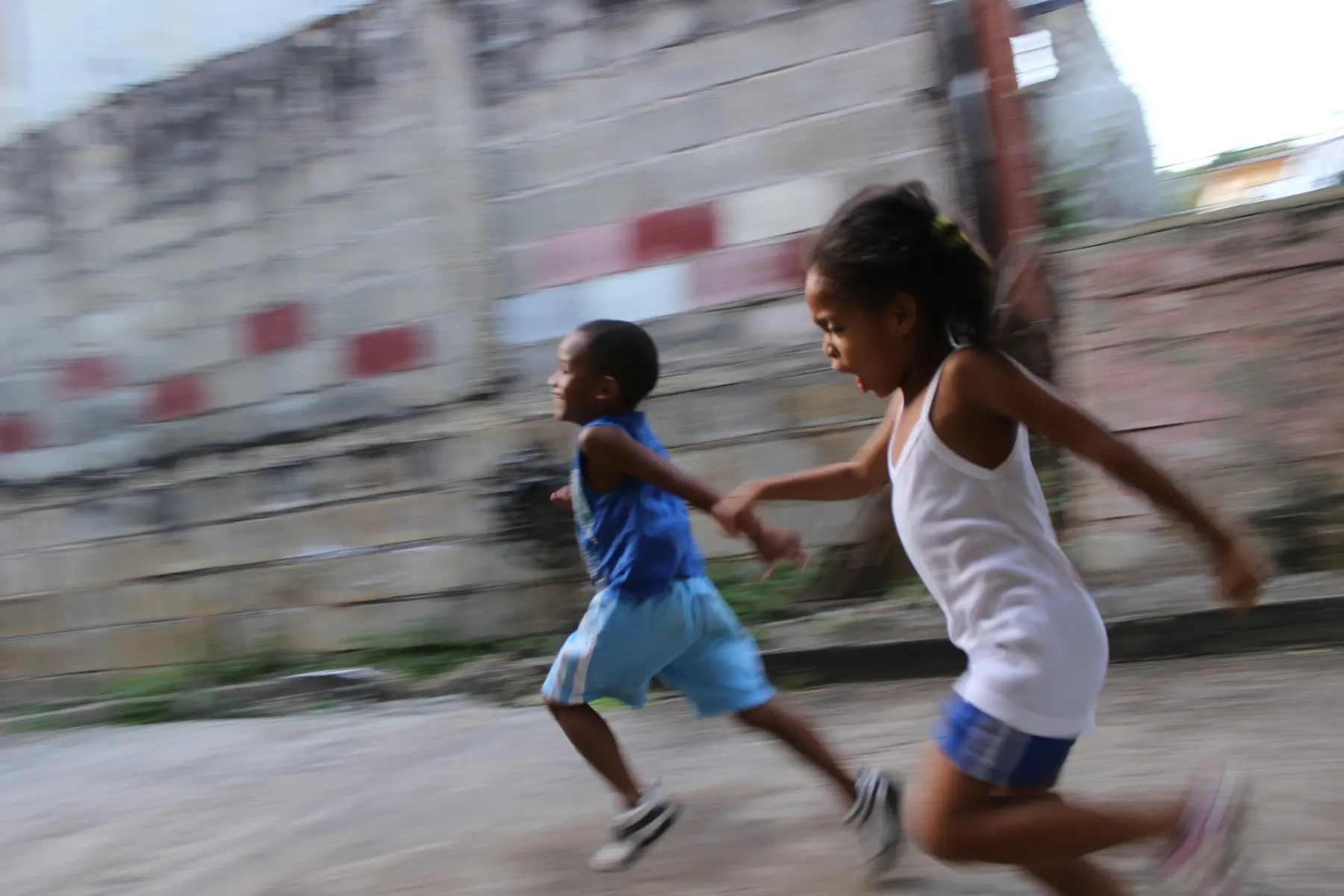 Two children running hand in hand along a sunlit street