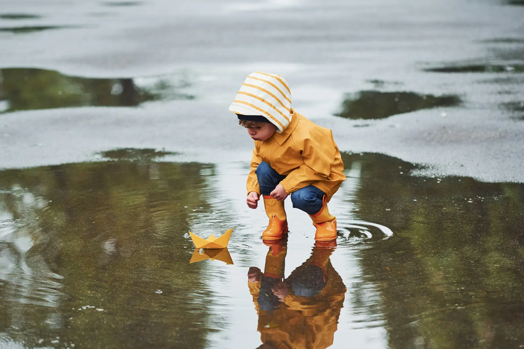 A child playing with a paper boat in a puddle